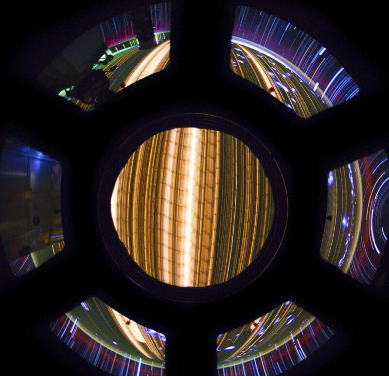 Circular space station window with colorful star trails and Earth lights in a long-exposure view
