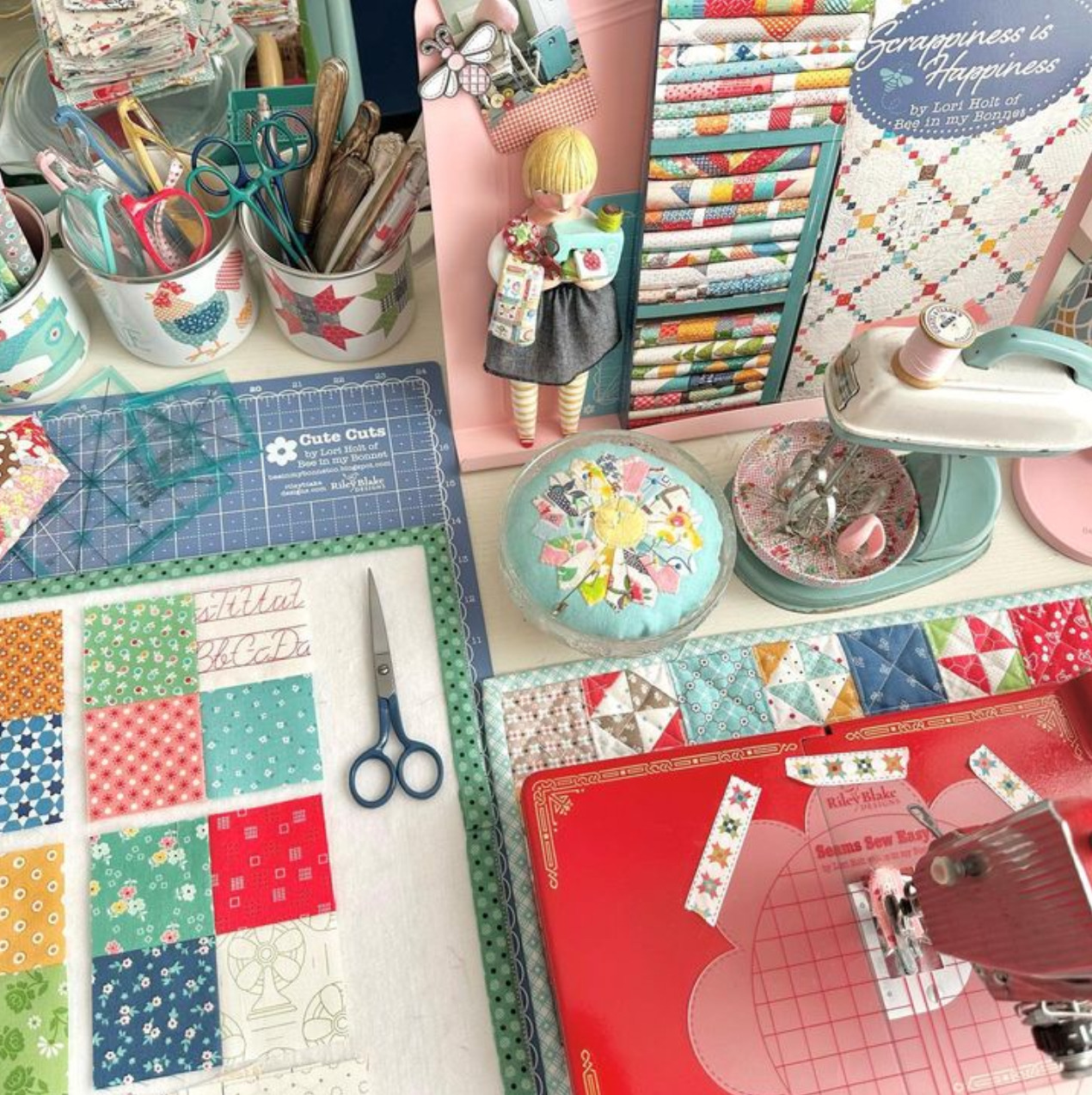 Quilting workspace with fabric swatches, cutting mat, sewing machine, and colorful craft supplies on a table