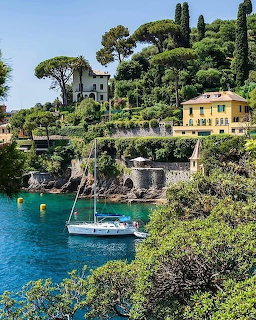 Sailboat mored in turquoise bay with colorful villas and green trees on hillside in Portofino, Italy