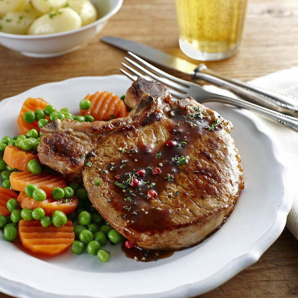 Bone-in pork chop with peas and sliced carrots on a white plate