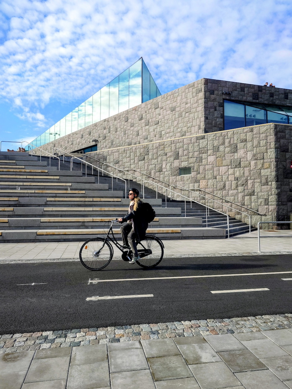 Cyclist passing the modern stone staircase and glass structure at Slussen, Stockholm
