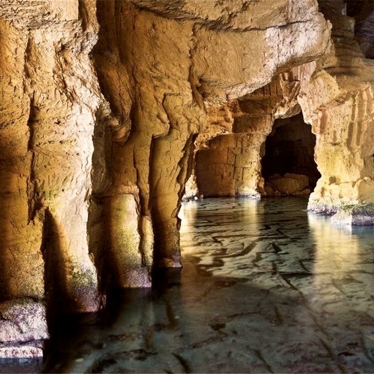 Illuminated underground cave with stone columns and reflective water pool