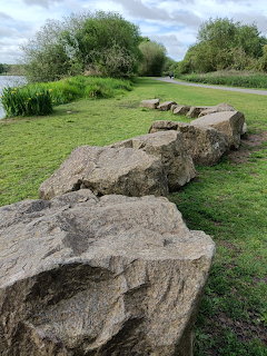 Row of large rocks snaking across green grass near a lake with trees in the background