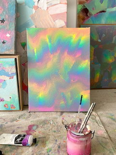 Holographic iridescent canvas with swirling pastel rainbow colors on an easel in an art studio