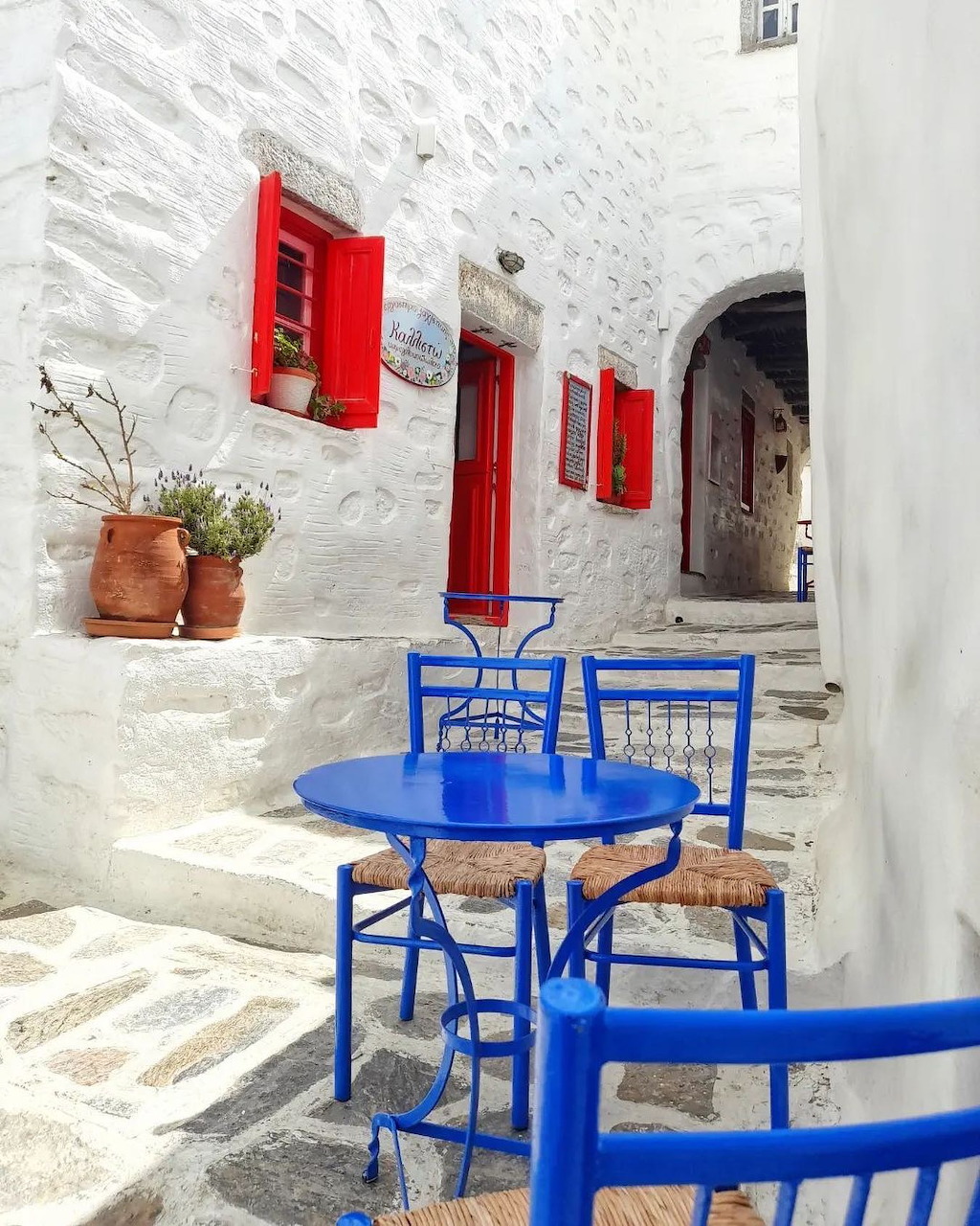 Blue outdoor furniture and red shutters on white building in Greek alley