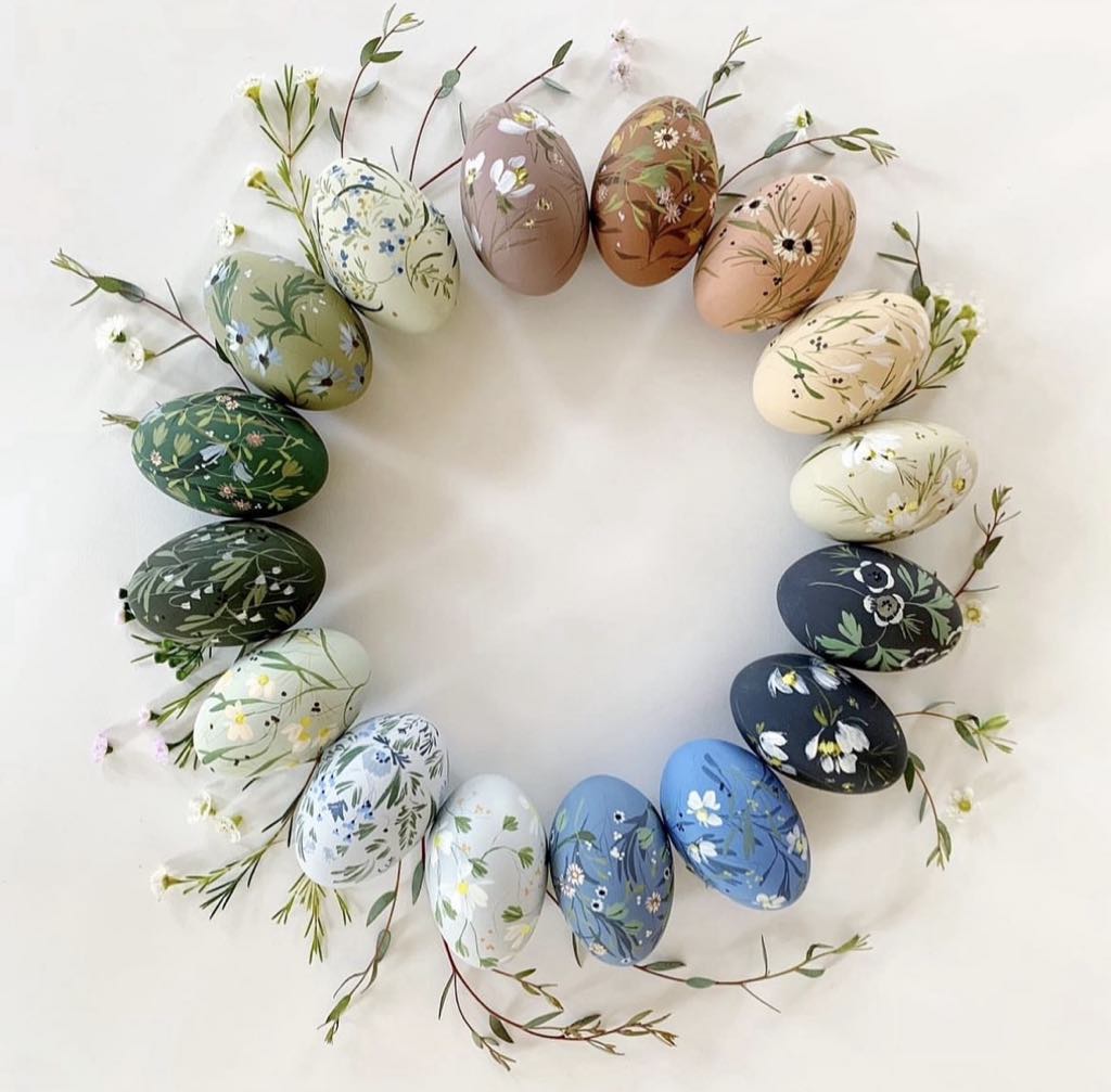Circular wreath of decorated Easter eggs with dried flowers arranged on white surface