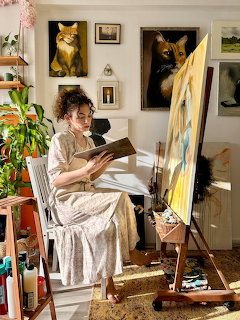 Woman reading a book next to an easel in a bright art studio with animal paintings on the walls