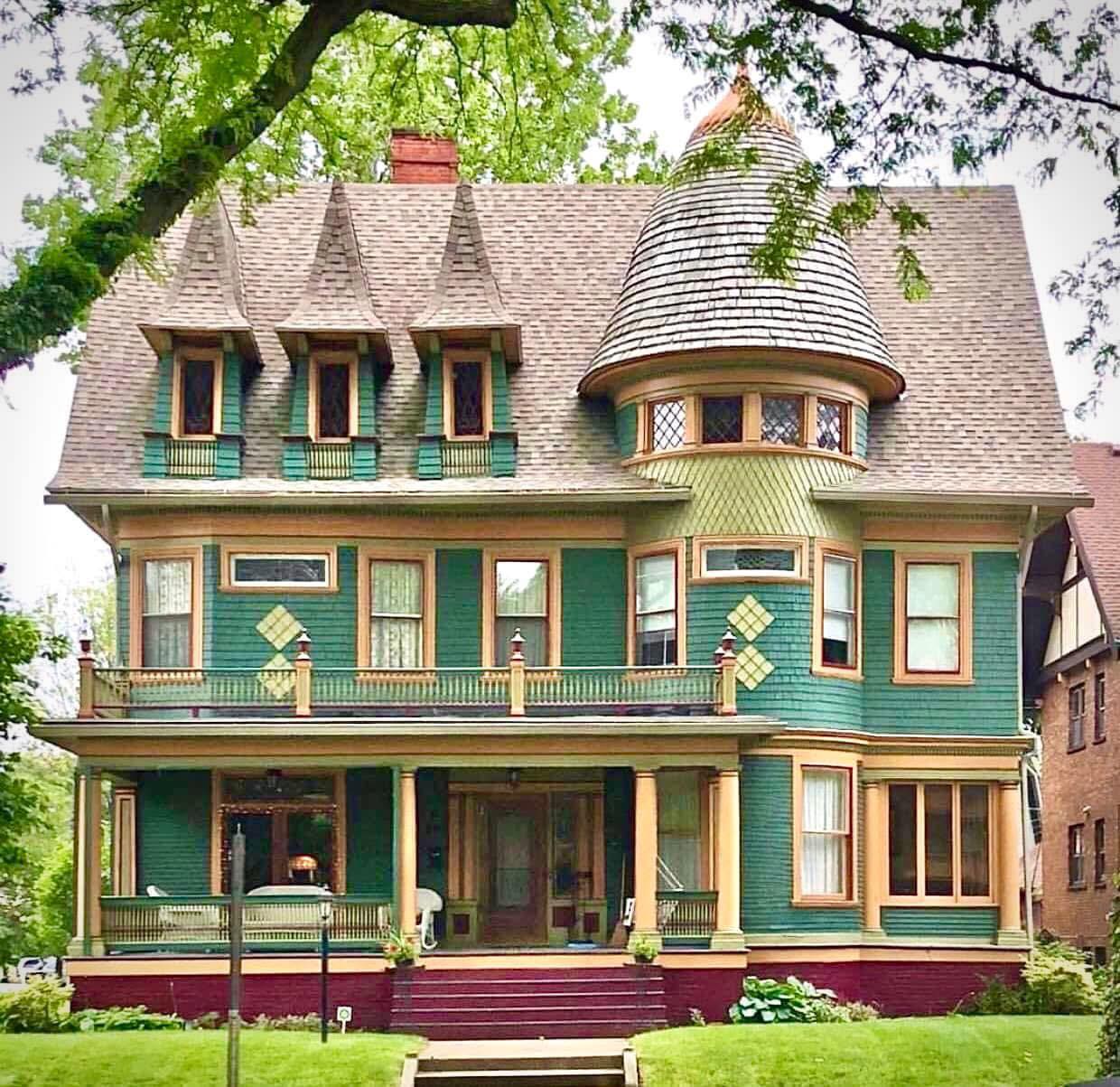 Victorian house with turret, green siding, burgundy accents, and front porch on green lawn