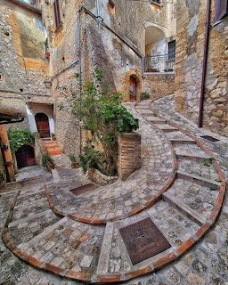 Spiral stone staircase with brick edges curving through a medieval village courtyard
