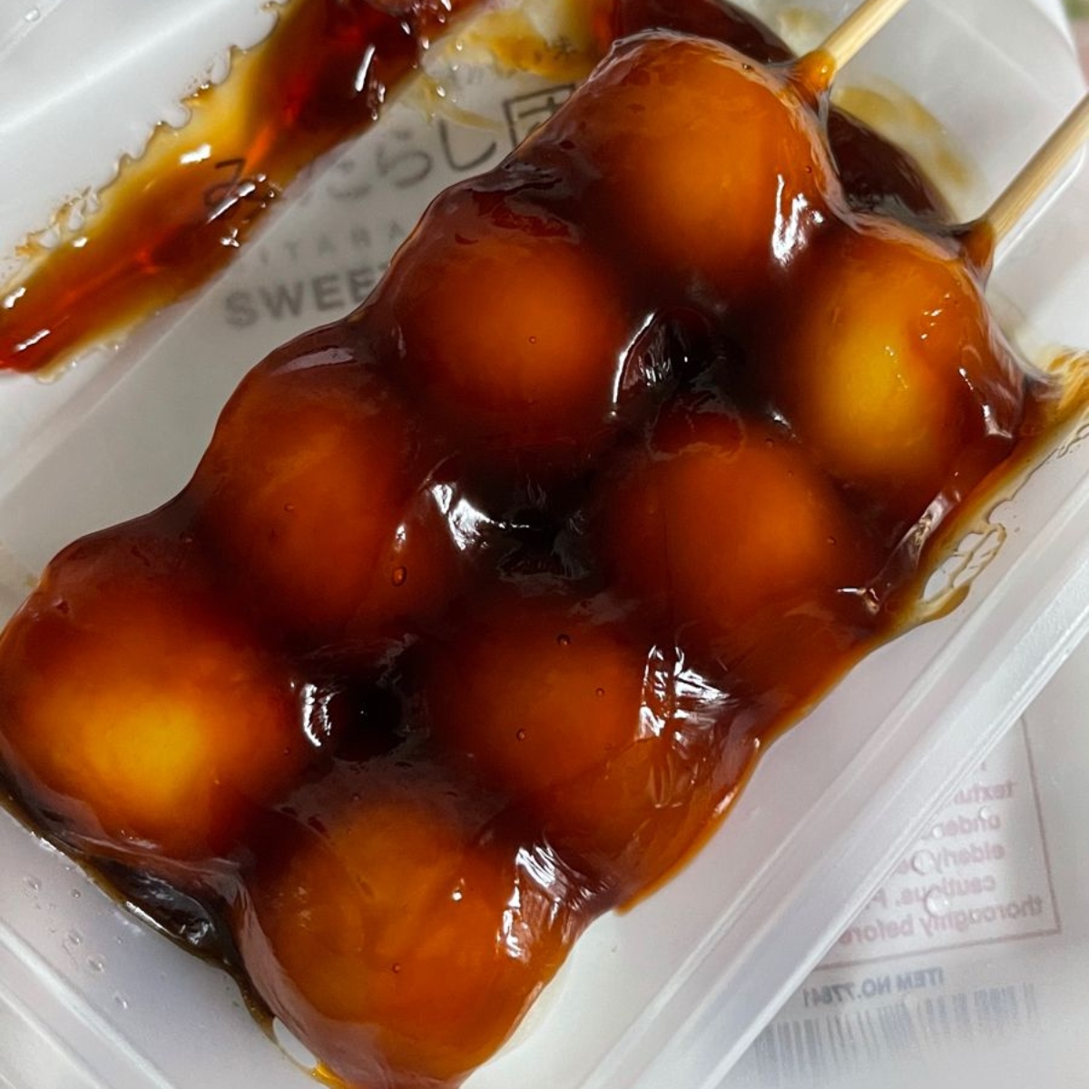 Skewered Japanese dango dumplings coated in glossy soy sauce glaze in a plastic tray