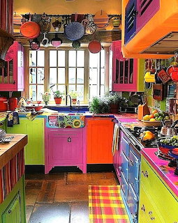 Bright eclectic kitchen with multicolored cabinets, hanging cookware, window with plants and checkered floor mat