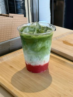 Layered drink with red strawberry, white cream, and green matcha in clear cup on wooden table