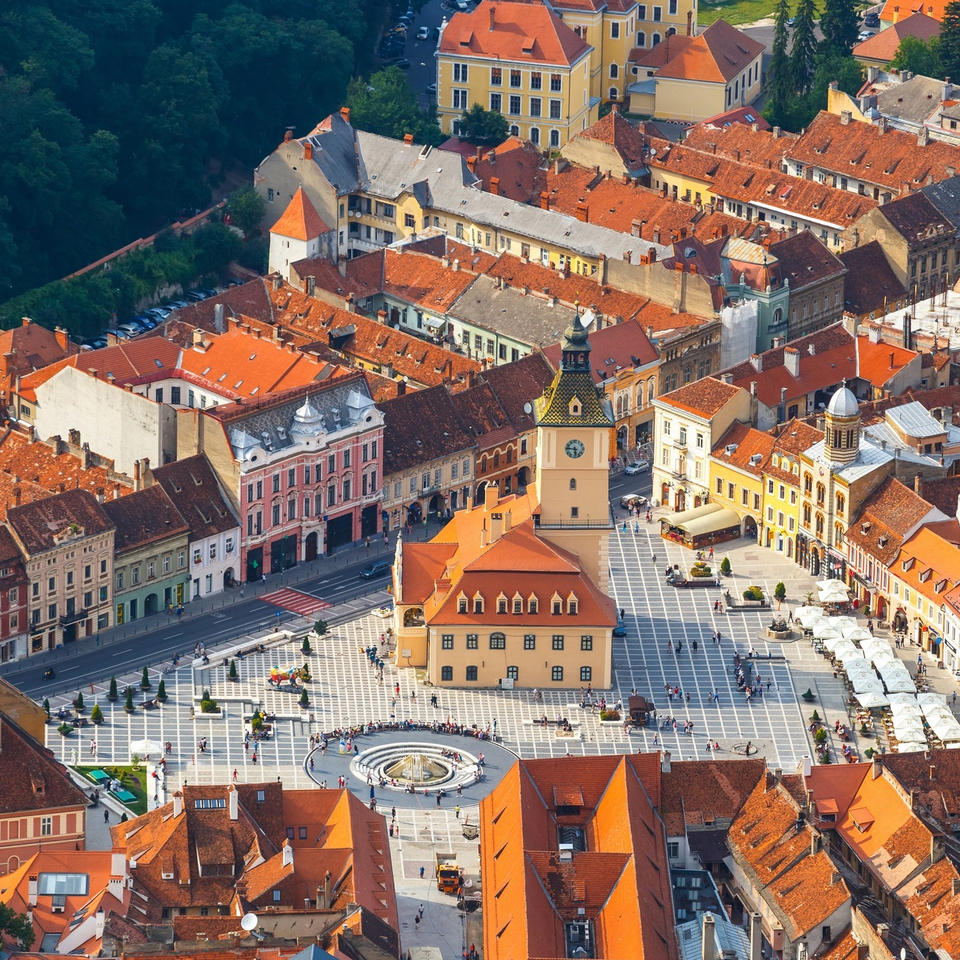 Aerial view of Brasov old town square with orange roofs, pastel buildings, and a clock tower