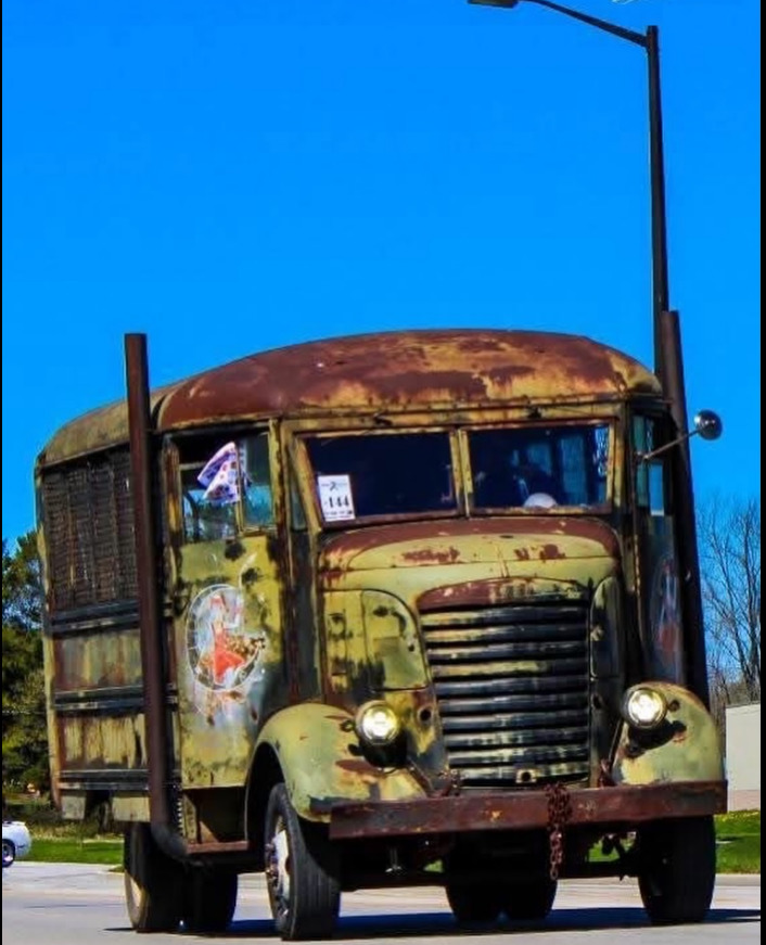 Rusty vintage COE cab-over-engine bus with green paint and weathered body driving on a sunny day