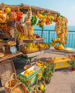 Rustic fruit stand with hanging lemons and tomatoes overlooking the Amalfi Coast sea