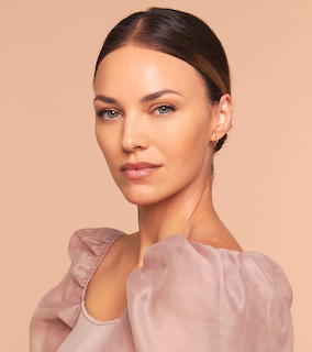Portrait of woman with dark hair in sheer beige top against peach background