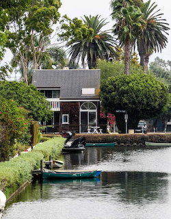 Dark wooden house beside a canal with turquoise boat and palm trees in Venice, California