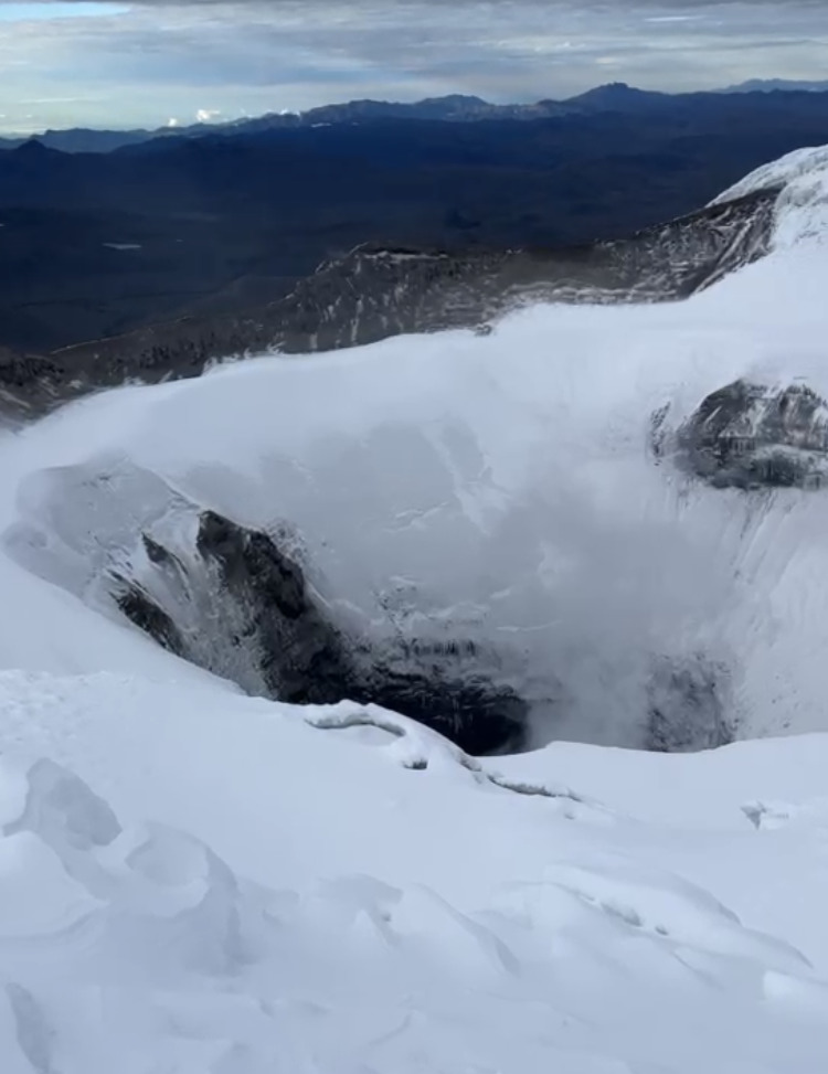 Snow-covered volcanic crater on Cotopaxi with distant dark mountains and cloudy sky
