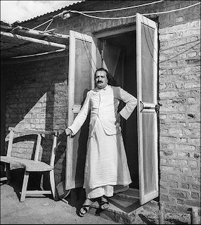 Meher Baba standing outside a hospital building in a vintage photograph