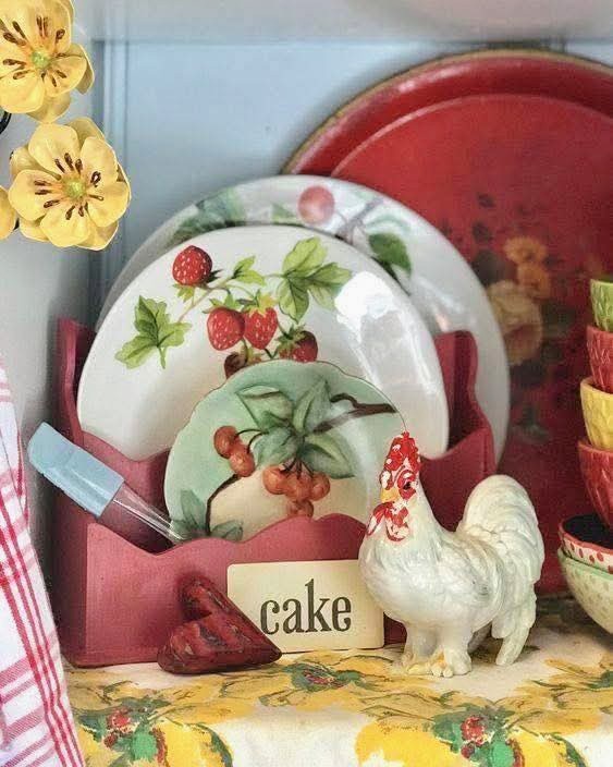 Vintage kitchen with fruit plates, red plate holder, ceramic rooster, and a 'cake' sign