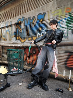 Young man in black fashion outfit posing with a golf club by a graffiti-covered wall