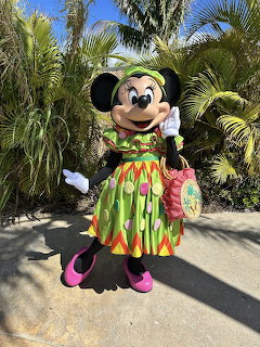 Minnie Mouse mascot wearing tropical outfit with grass skirt and lei in front of palm trees
