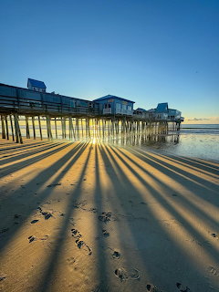Wooden pier casting long shadows across a sandy beach by calm ocean water