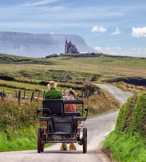 Horse-drawn jaunting car on a narrow Irish country road heading toward a church and mountains