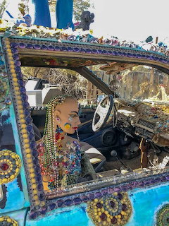 Mannequin head with beads and jewelry displayed in colorful mosaic car window frame at outdoor art installation