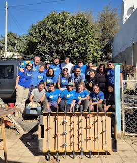 Large group of volunteers in blue shirts posing together outdoors at a community project site