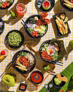 Flatlay of colorful brunch dishes including eggs, vegetables, bread, and drinks on checkered tablecloth
