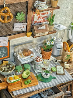 Detailed miniature bakery cafe diorama with tiny pretzels, macarons, pastries, plants, and kitchen items