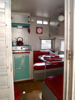 Vintage RV trailer interior with turquoise cabinets, red seating, and retro appliances