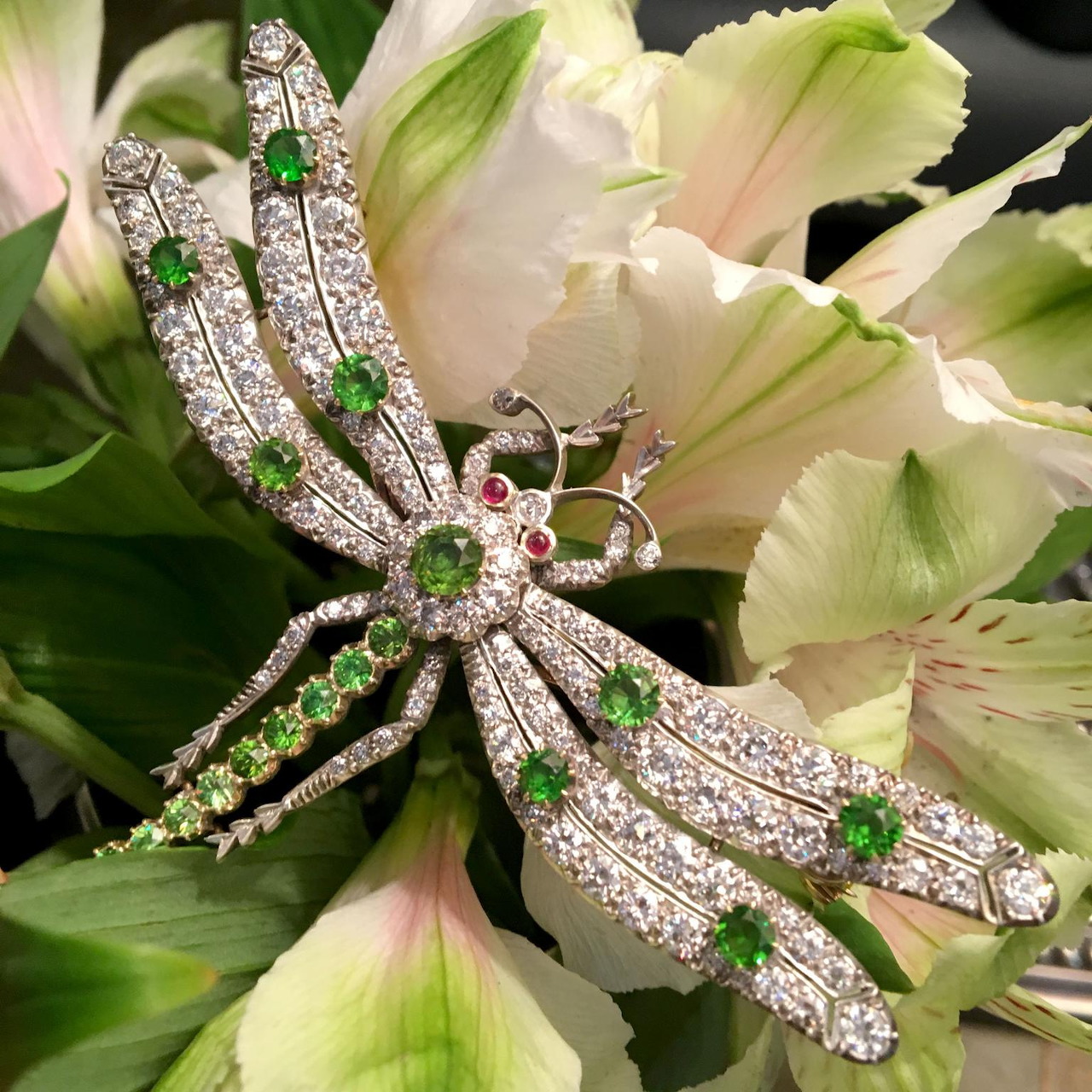 Silver dragonfly brooch with green and pink gemstones on white flowers