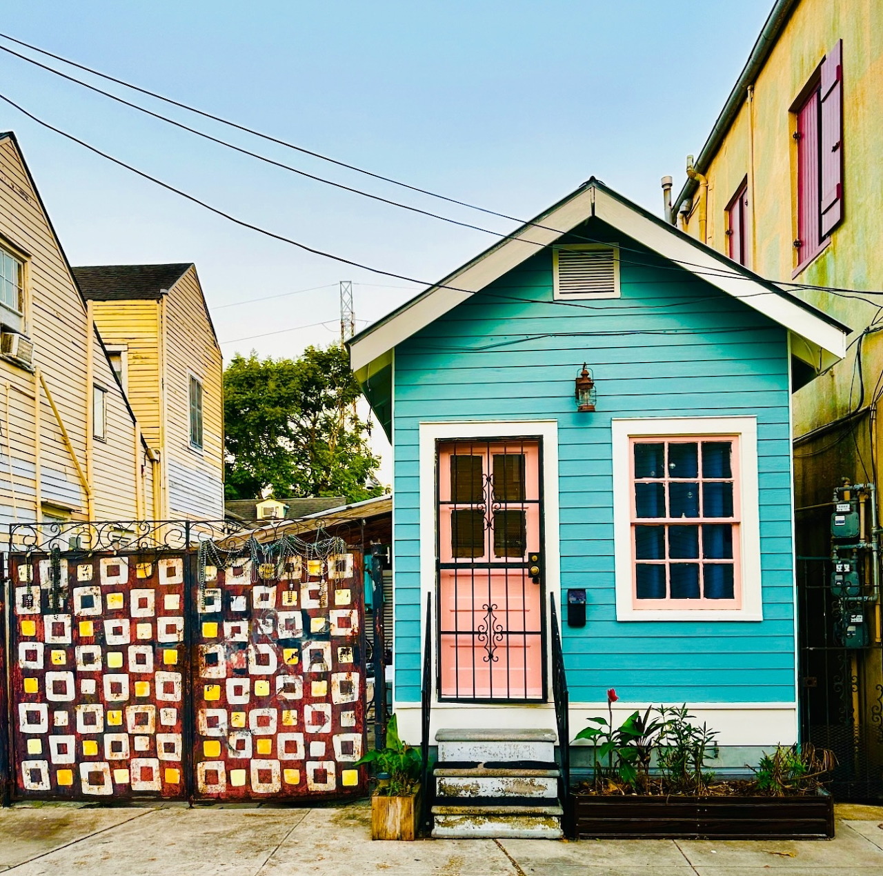 Turquoise tiny house with pink door and a patchwork quilt hanging on a fence in a neighborhood