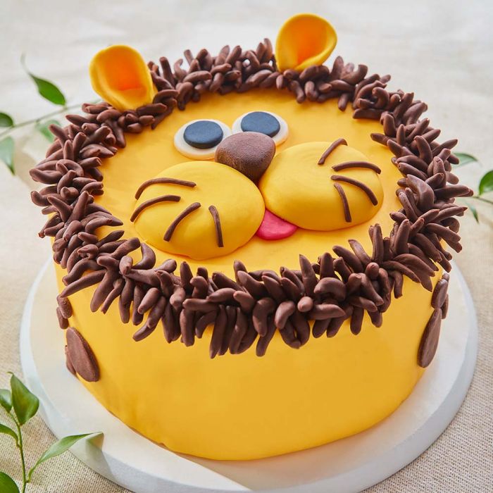 Yellow lion face cake with a chocolate mane and whiskers on a white cake board