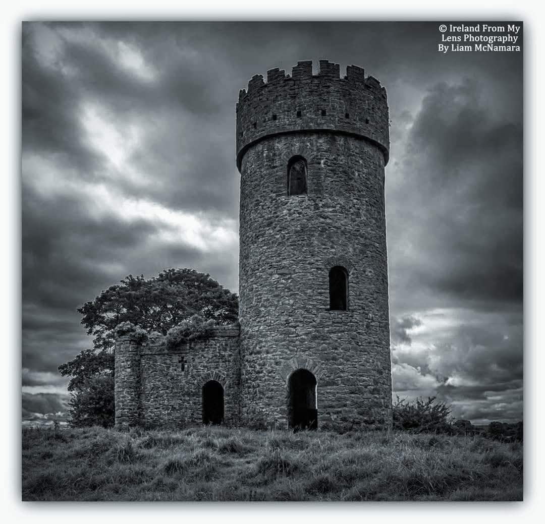 Black and white stone castle tower with ruined walls beneath dark clouds