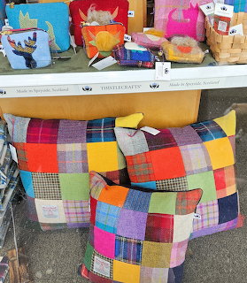 Colorful patchwork cushions and tartan fabrics displayed on wooden shelf outside Scottish shop