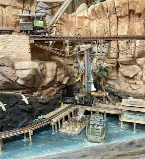 Boat in blue water below railroad tracks and wooden platforms in a rocky mine setting
