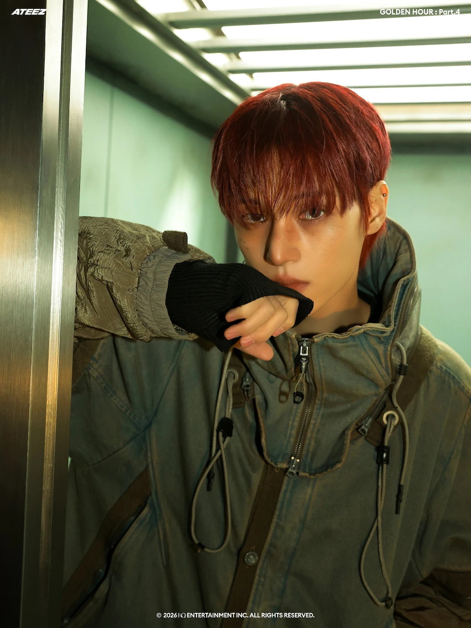 Young man with red hair in a green jacket posing in an elevator for Ateez Adrenaline concept
