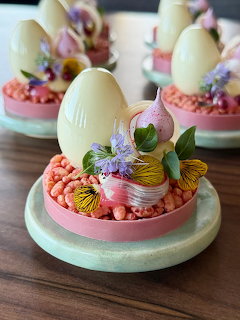 White chocolate egg desserts with edible flowers and butterflies on pink and mint green bases