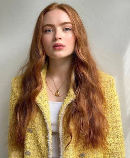 Young woman with long red hair in yellow cardigan looking at camera