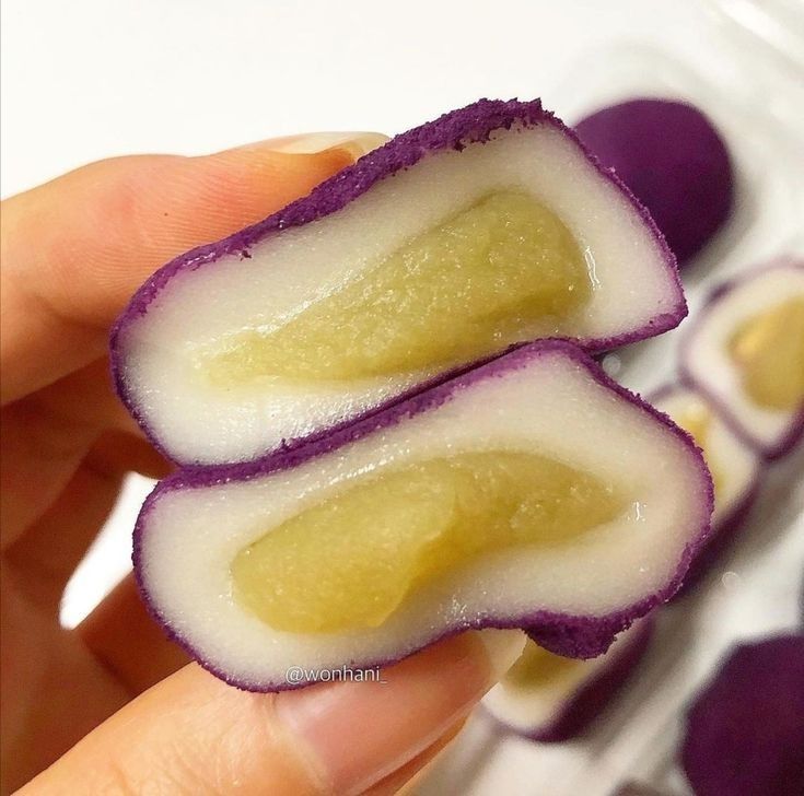 Hand holding cut purple sweet potato mochi with white layer and yellow filling