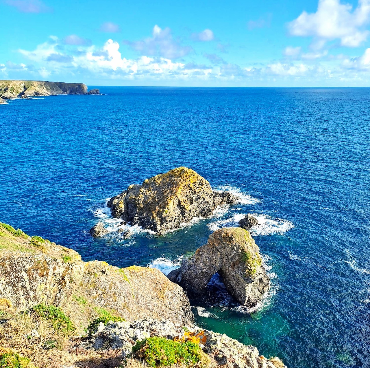 Rocky coastal cliffs and small islands in bright blue ocean water with white clouds above