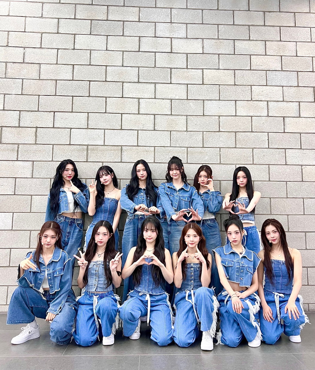 Group of young women in denim outfits posing together against a concrete wall