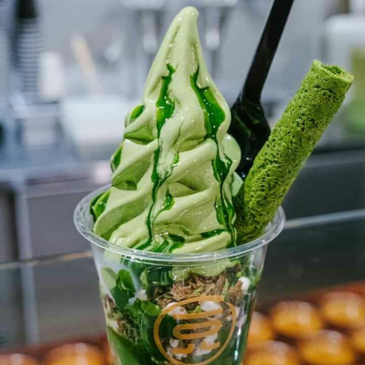 Cup of matcha soft serve ice cream with green syrup and a matcha wafer stick