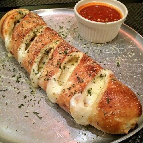 Sliced garlic bread on a metal tray with herbs and a cup of red dipping sauce