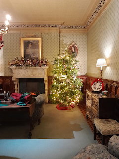 Victorian-style room with a lit Christmas tree beside a fireplace