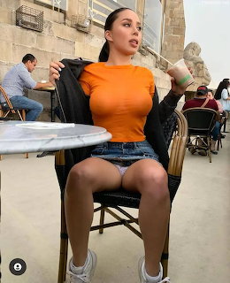 Woman sitting in chair wearing orange top and denim shorts at outdoor café