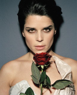 Dark-haired woman in white satin top holding a red rose close to her face in a studio portrait